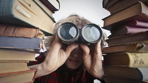 using binoculars to look through a pile of books
