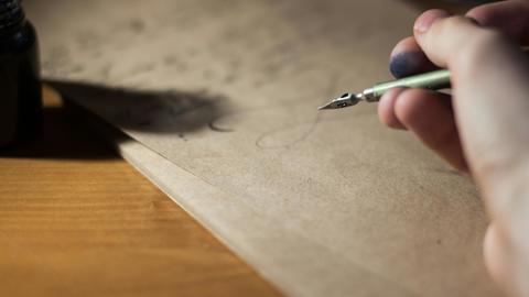 ink stained hand holding fountain pen over parchment