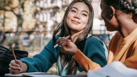 two women students studying outdoors in sunshine