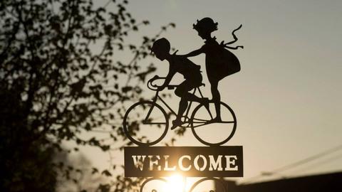 Welcome sign with two children riding a bicycle with the sun rising behind