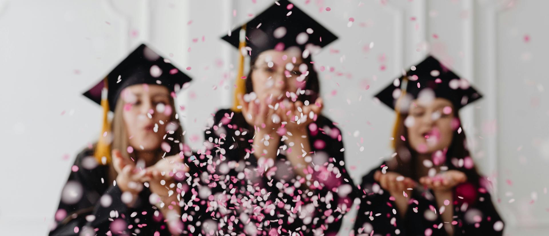 three happy graduates blowing confetti around them