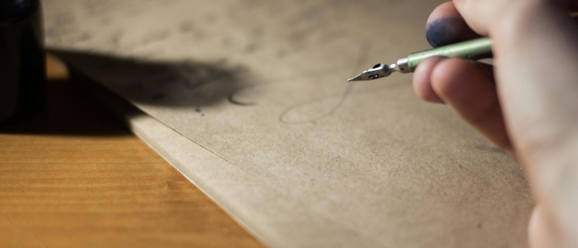 ink stained hand holding fountain pen over parchment