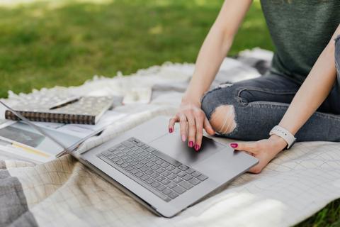 woman working on computer on picnic blanket in park